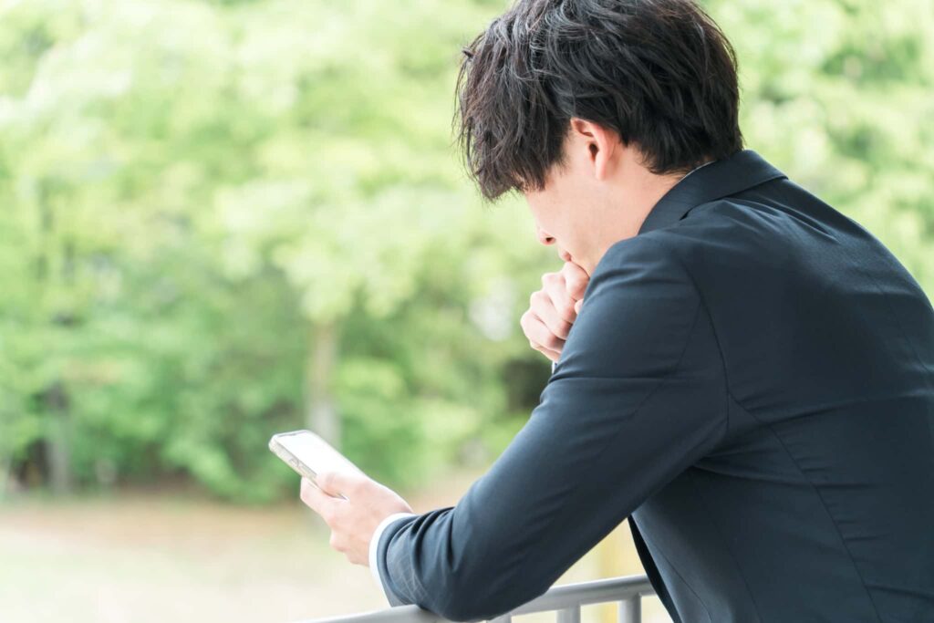スマホを見て悩む男性のイメージ