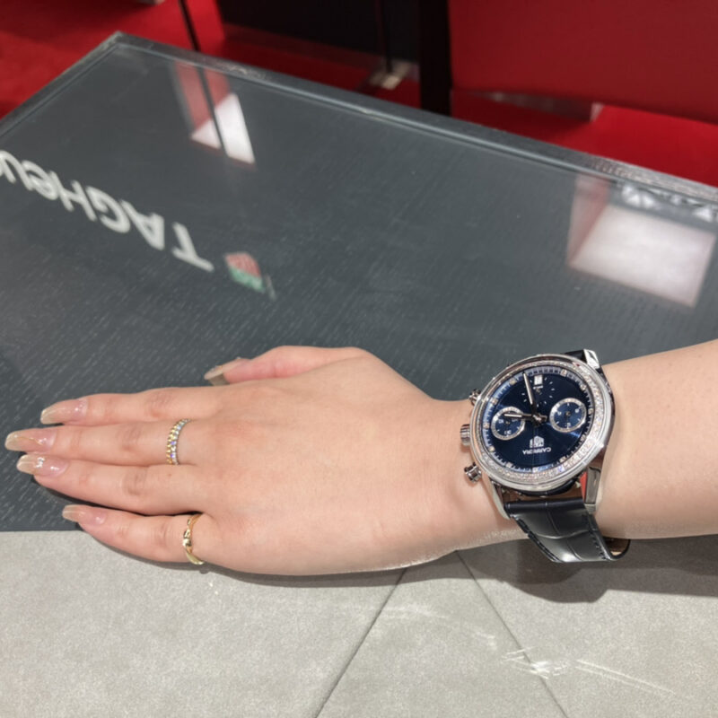 「TAG Heuer」ロゴとカレラ クロノグラフ ダイヤモンド［品番：CBS2214.FC6567］を着装する女性の腕元